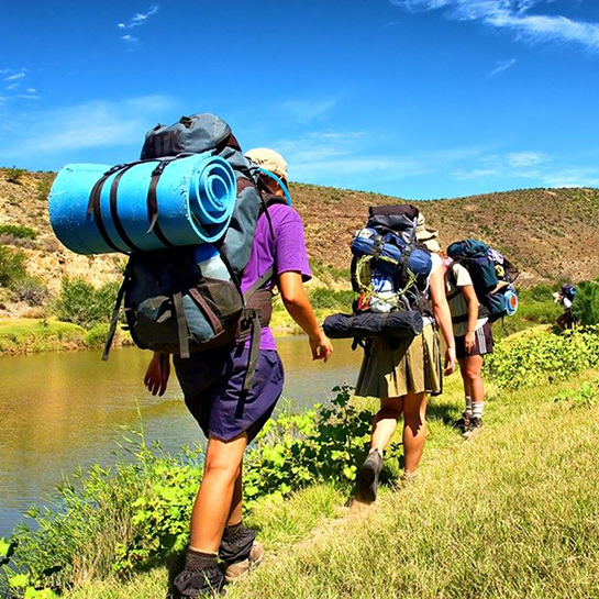 Three hikers with backpacks on a trail.