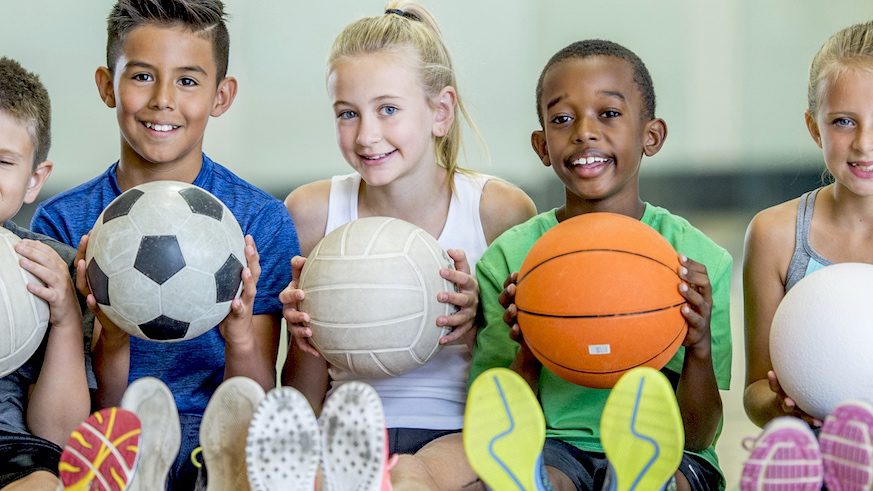 Smiling kids holding different sports balls.